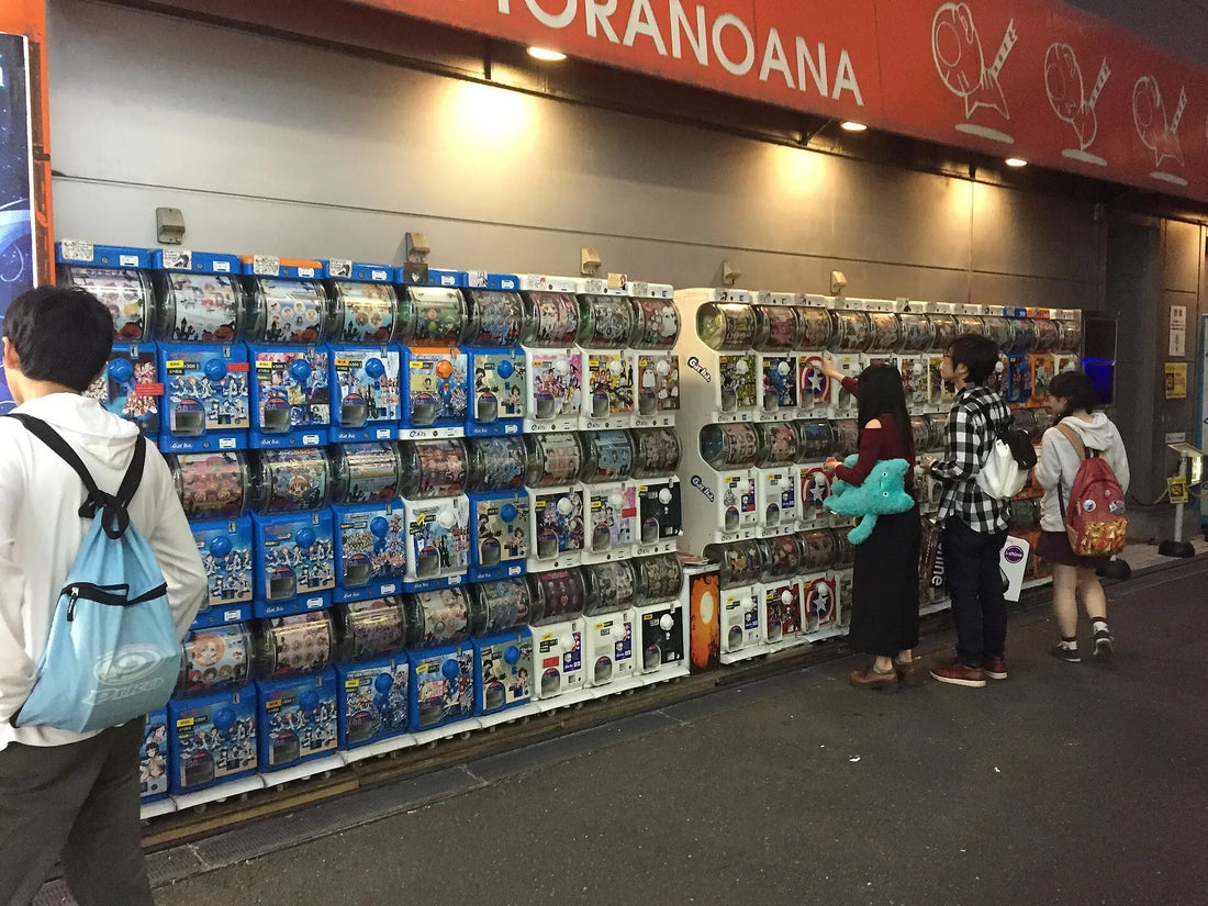 A wall of capsule-toy machines outside a shop in Akihabara, Tokyo, with people turning the handles