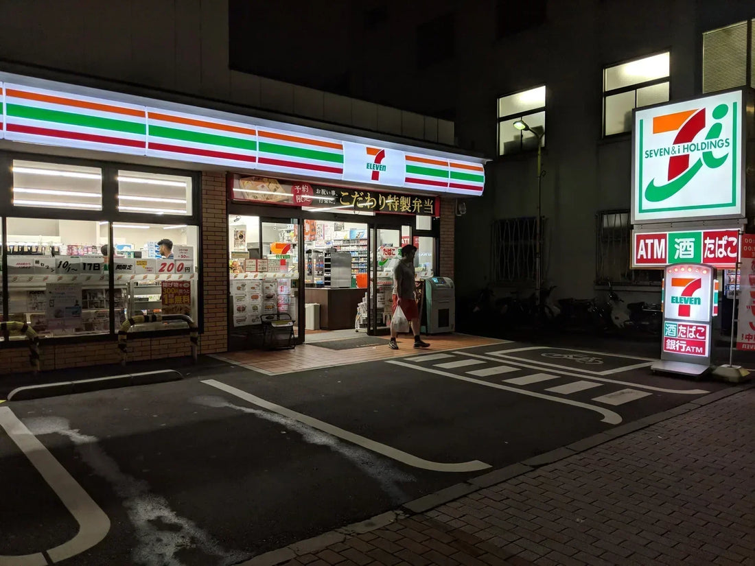 A 7-Eleven in Tokyo at night, its stripe lit above the doorway