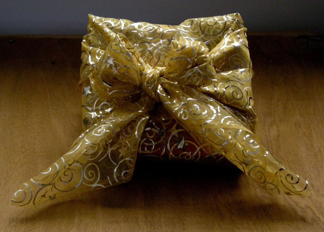 A present wrapped in a gold patterned furoshiki cloth, tied in a knot on top