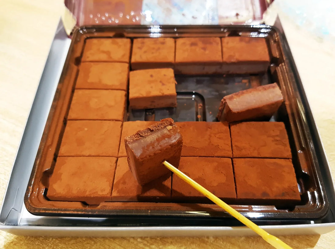 Nama chocolate — an open box of cocoa-dusted squares, one lifted on a pick to show its soft cut face