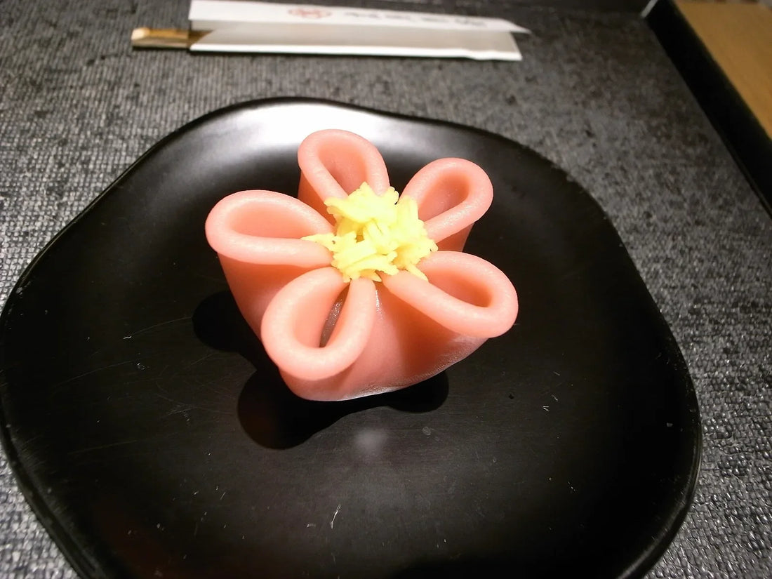 A pink five-petalled fresh sweet with a yellow centre, on a black plate at Toraya Café in Japan